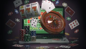 Online casino concept. Laptop with roulette, slot machine, casino chips and playing cards isolated on black background. 3d illustration