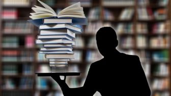 A man balancing a heap of books in one hand.