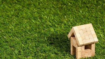A wooden toy house placed on the grass.