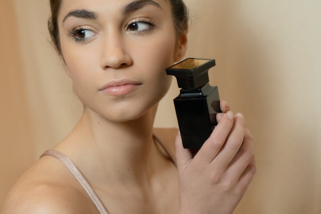 Woman holding a black perfume bottle near her cheek.