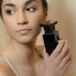 Woman holding a black perfume bottle near her cheek.