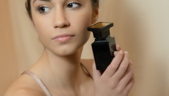 Woman holding a black perfume bottle near her cheek.