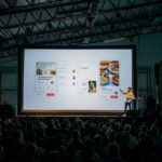 A man presenting on the screen in an event.