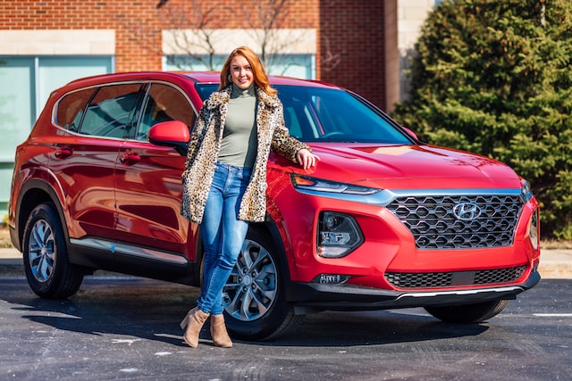 A woman posing near a red car.