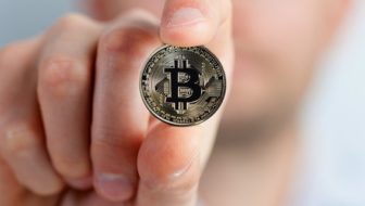 A man holding a Bitcoin between his fingers.
