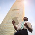 An Entrepreneur holding papers in his hand near a sky scraper.