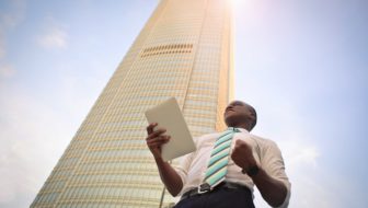 An Entrepreneur holding papers in his hand near a sky scraper.
