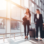 Two women travelling holding luggage in their hands.