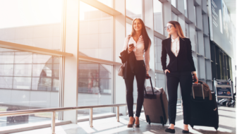 Two women travelling holding luggage in their hands.